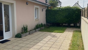A residential property with a paved patio, a door leading to a covered entrance, and a well-maintained hedge.