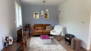A living room with a sofa, a white armchair, a patterned rug, and a small table with a television.