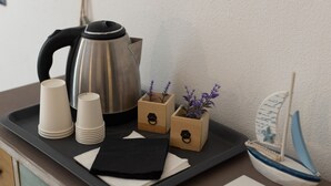 Un plateau contenant une bouilloire, des gobelets en papier, des serviettes et une petite décoration en forme de bateau, posé sur un comptoir.