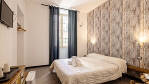 Une chambre d’hôtel avec un lit, un téléviseur fixé au mur, une commode en bois et une fenêtre avec des rideaux.