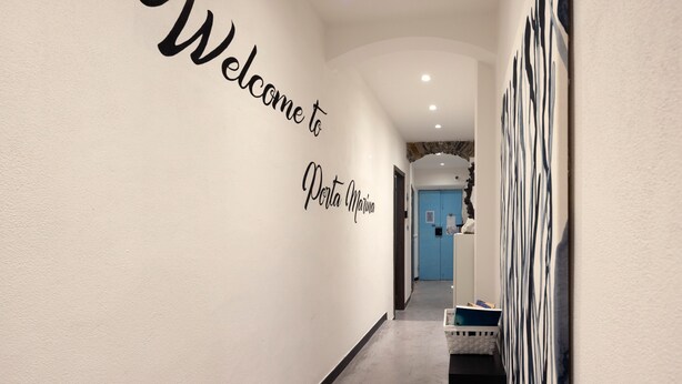 Un couloir avec une pancarte indiquant « Bienvenue à Porto Marinho », une porte bleue et un mur orné d’œuvres d’art abstrait.