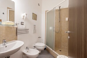 A bathroom with a sink, toilet, bidet, and a glass-enclosed shower.