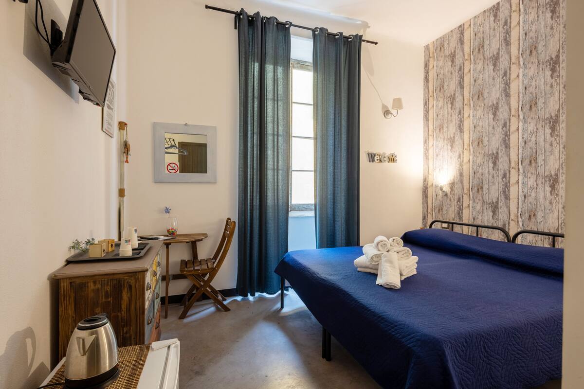 Une chambre d’hôtel équipée d’un lit, d’un bureau avec une bouilloire, d’une chaise et d’un téléviseur fixé au mur.