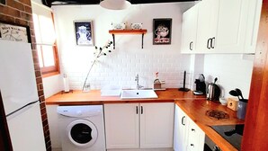 Una cocina compacta con armarios blancos, lavadora, pileta y estufa.