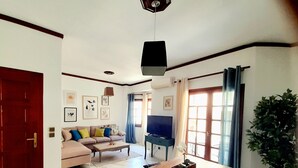 Una sala de estar con un sofá, una mesa de comedor de madera, un televisor y una planta en maceta.