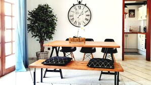 Un comedor con una mesa de madera, sillas negras, una planta en maceta y un reloj de pared.
