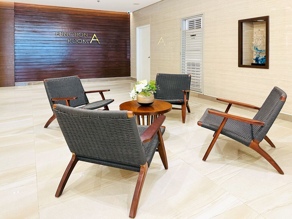 A lobby with four wicker chairs around a round table, a wooden wall with a sign, and a framed artwork on the wall.