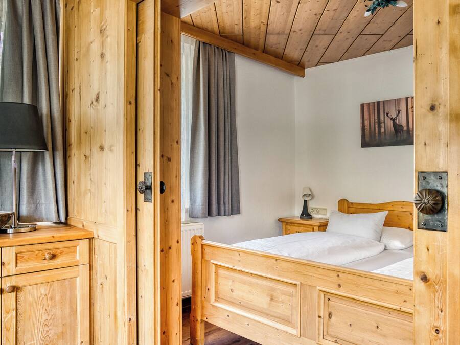 A wooden room with a bed, a nightstand, a lamp, and a window with curtains.