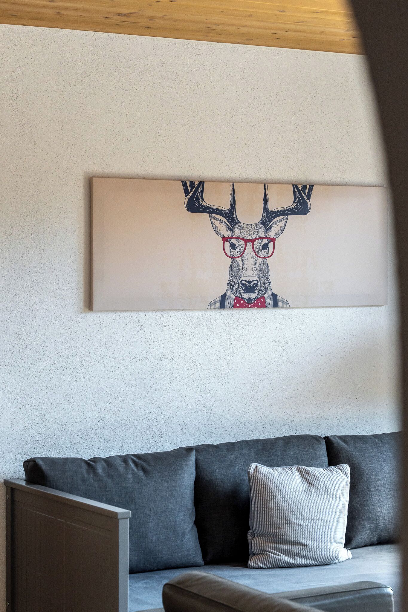 Ein modernes Wohnzimmer mit einem grauen Sofa und einem gerahmten Kunstwerk, das einen Hirsch mit Brille zeigt.