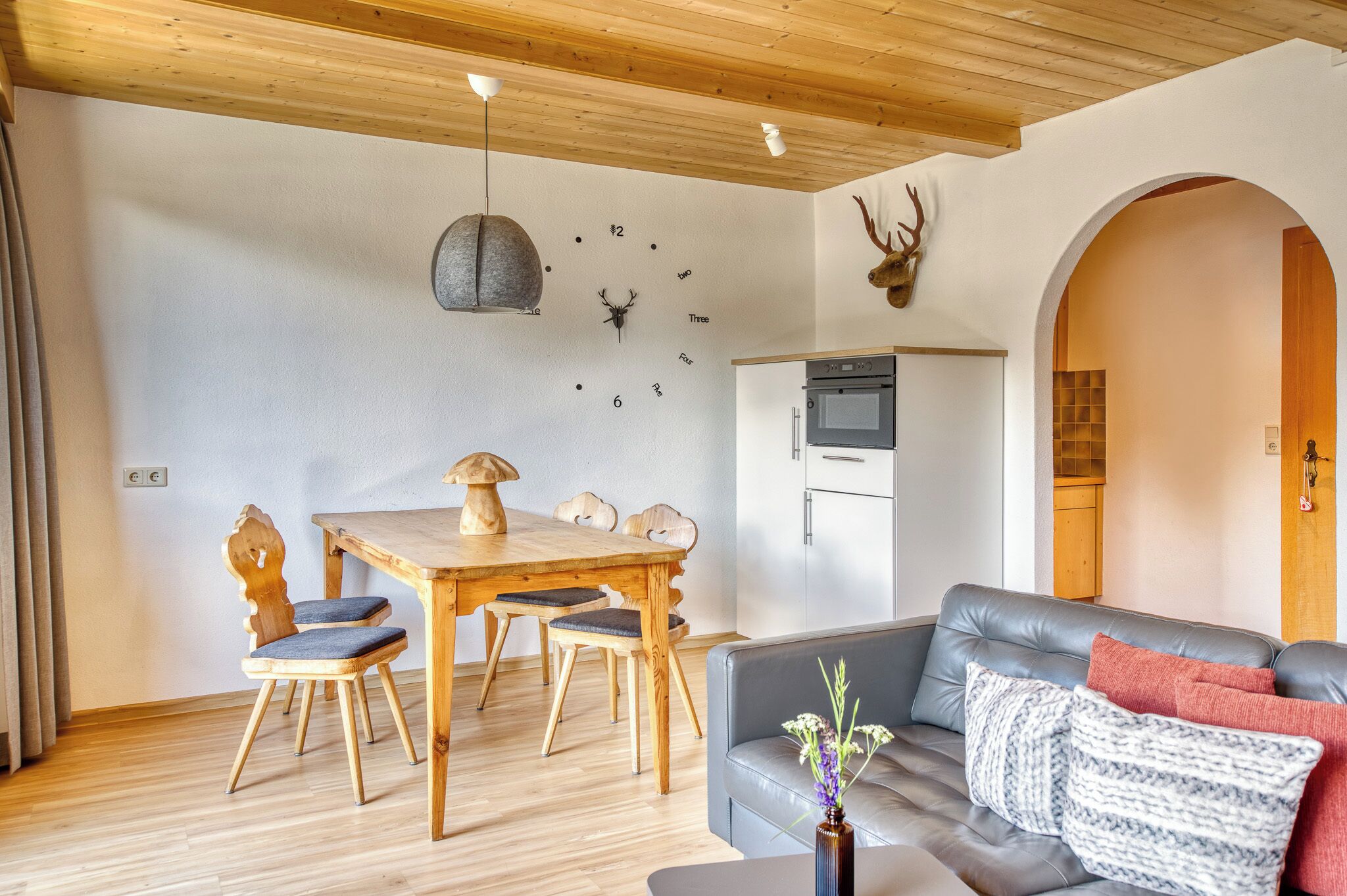 Una sala de estar moderna con una mesa de comedor de madera, un sofá gris y un reloj de pared decorativo.