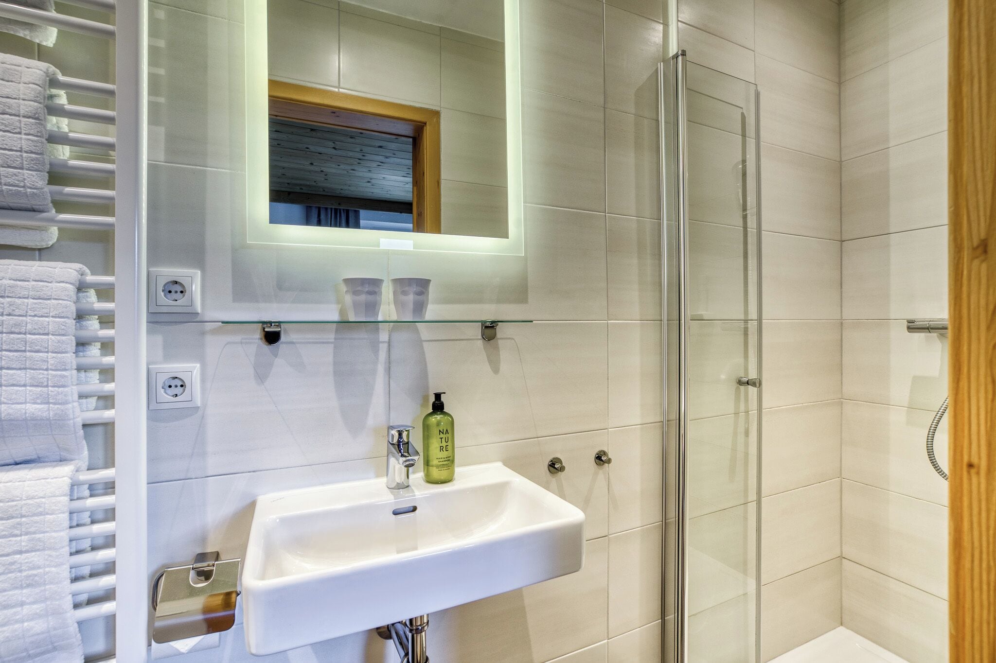 A modern bathroom with a glass shower enclosure, a white sink with a mirror above it, and a towel rack with folded towels.