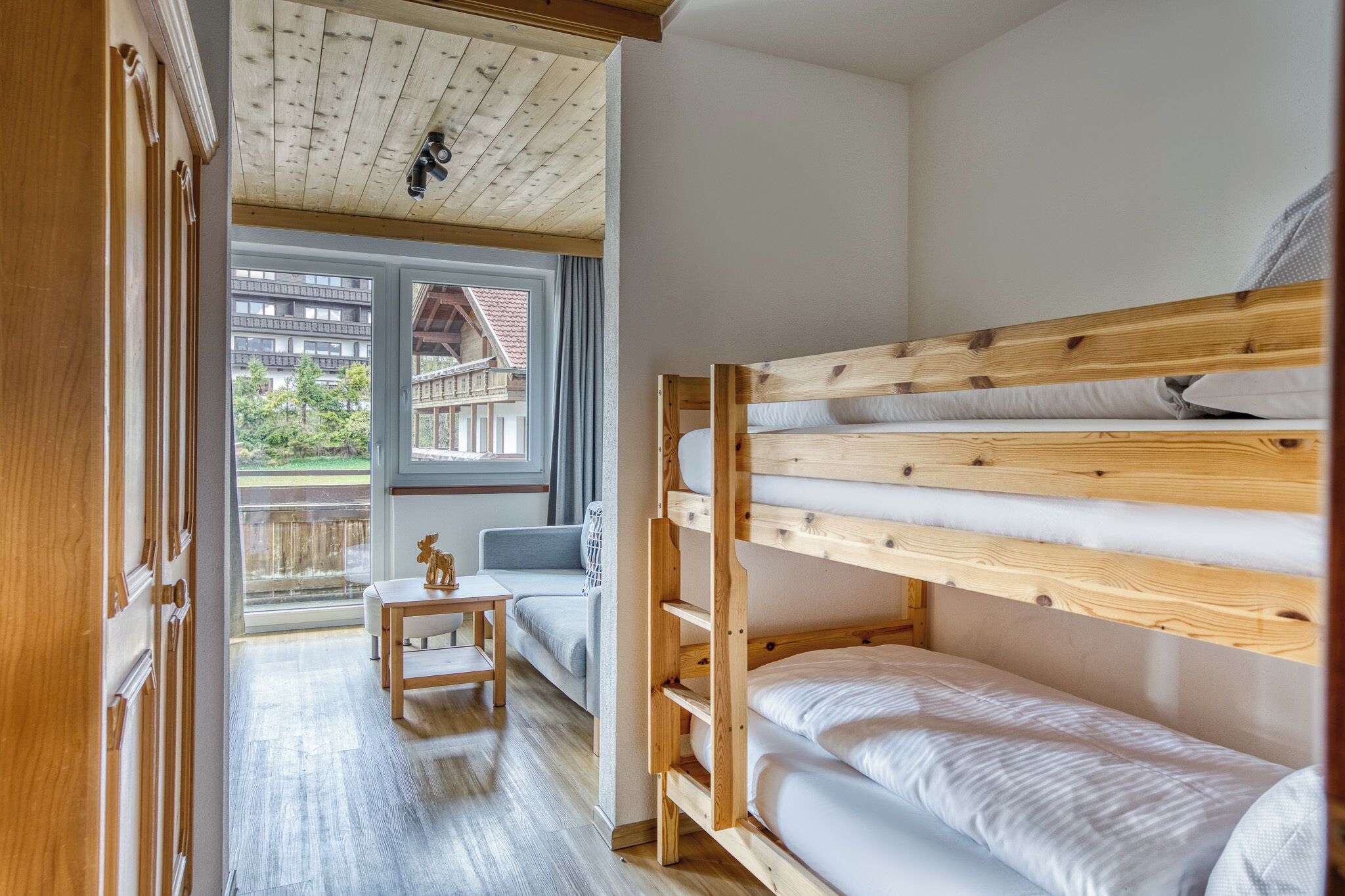 A room with a bunk bed, a sofa, a small table, and a view of a building outside.