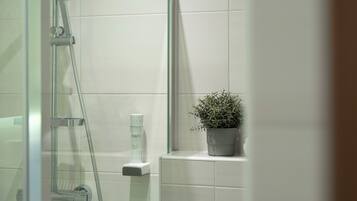 A shower with a glass door, a potted plant on the wall, and a soap dispenser.