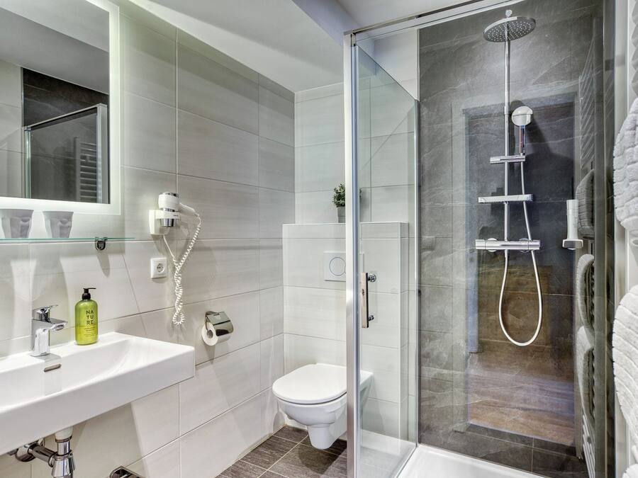 Un baño moderno con cabina de ducha de vidrio, un lavabo blanco con espejo y un inodoro.