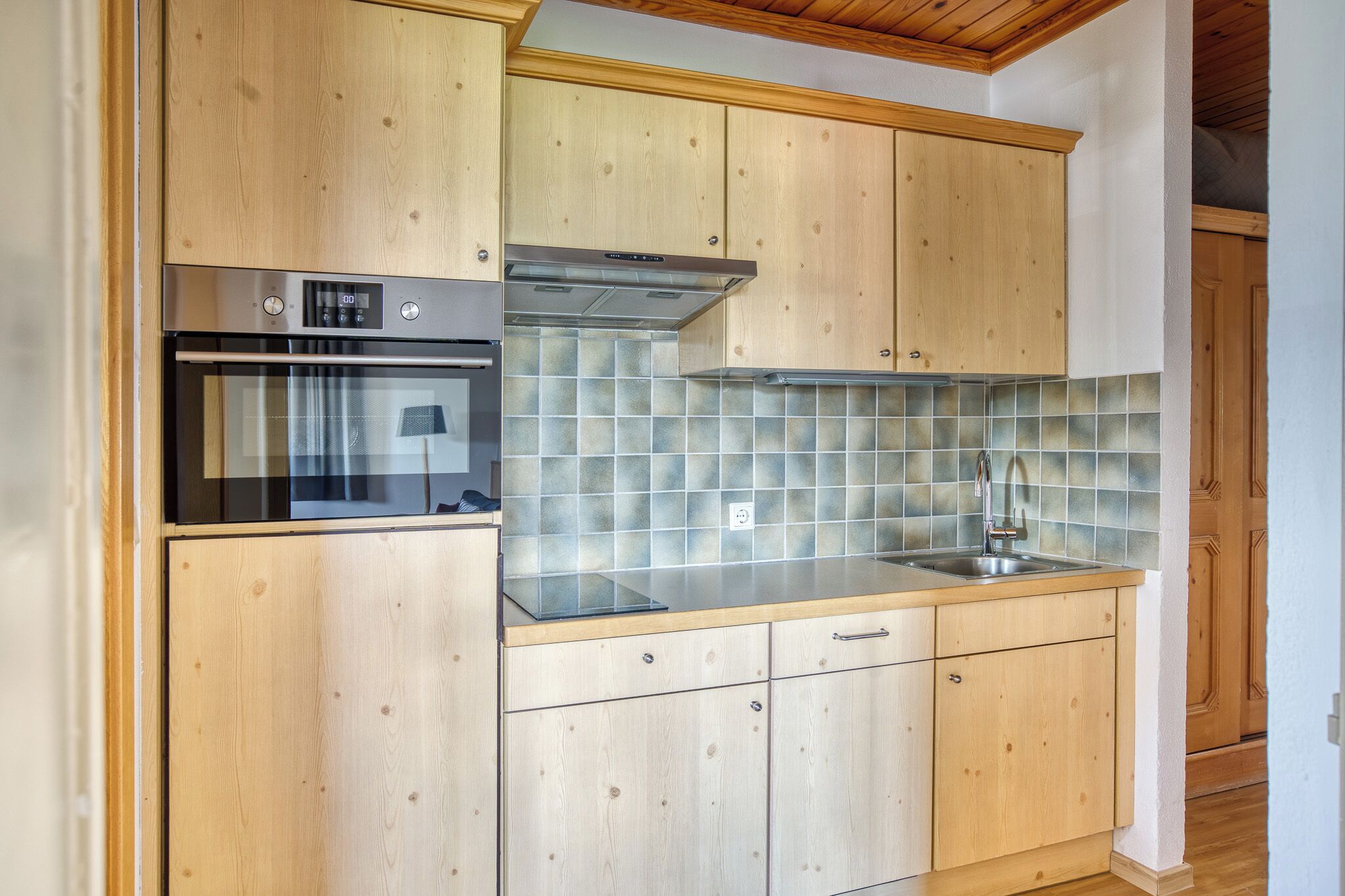 Una cocina con armarios de madera, horno de acero inoxidable, salpicadero de azulejos y un lavamanos.