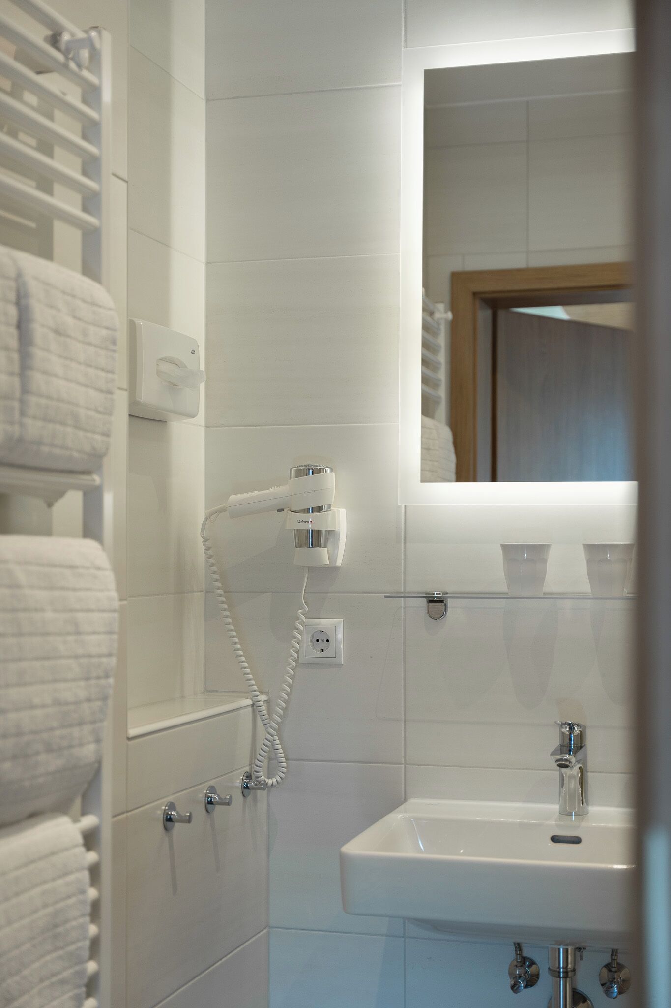 Un baño con lavamanos blanco, espejo y perchero.