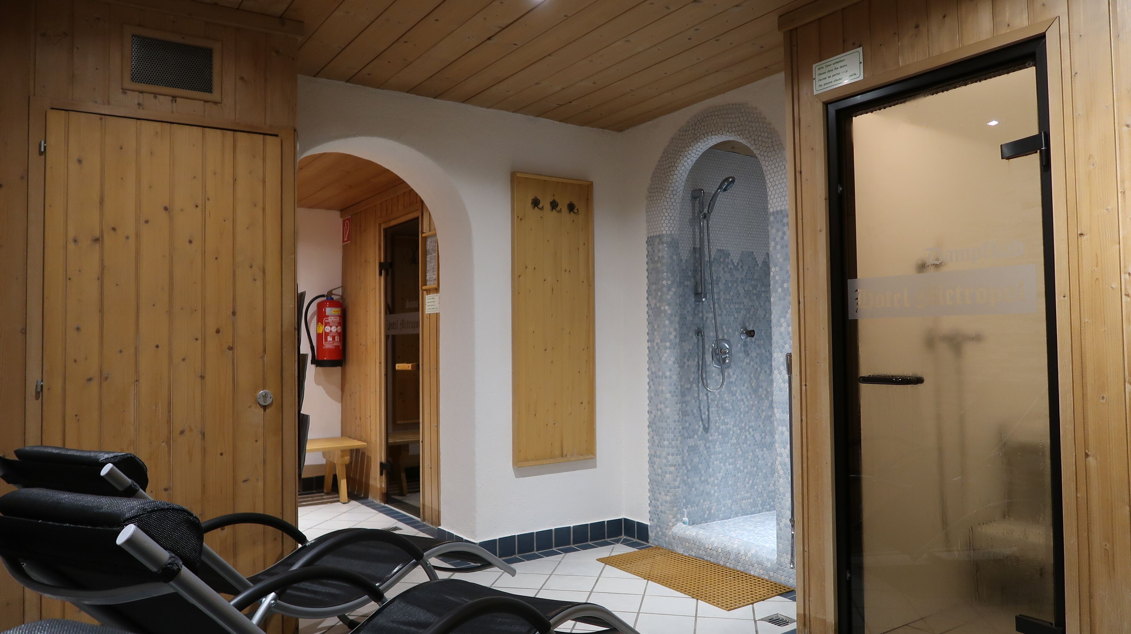 Un cuarto de sauna con paredes de madera, piso de baldosas y puerta de vidrio que da a una zona de ducha.