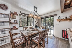 A dining area with a wooden table set for four, surrounded by wooden chairs with cowhide upholstery. A chandelier hangs above the table, and there are wooden shelves with various items on the walls. - Ridgeview Retreat ~ Where Location Meets Comfort (AC!) (Shaver Lake)