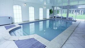 An indoor swimming pool with clear glass walls, a tiled floor, and a potted plant near the windows.