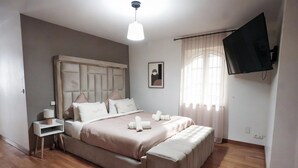 A bedroom with a bed, bedside table, lamp, and a TV mounted on the wall.