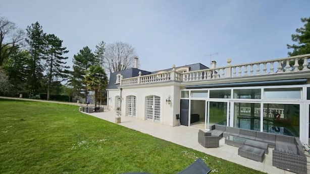 A large house with a spacious lawn, a covered patio area, and a swimming pool.