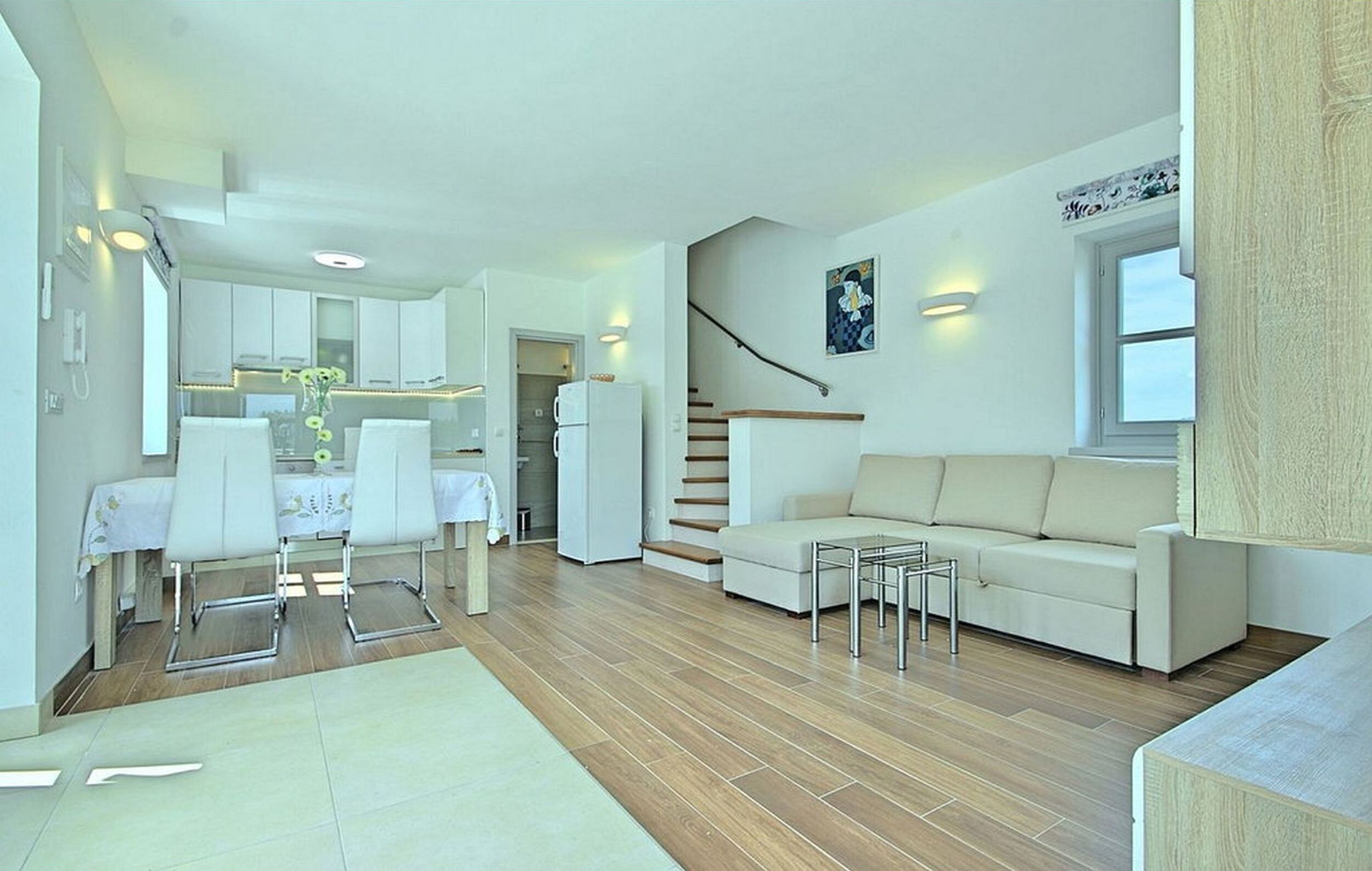 Una sala de estar moderna con un sofá, una mesa de comedor con sillas, una escalera y una zona de cocina.