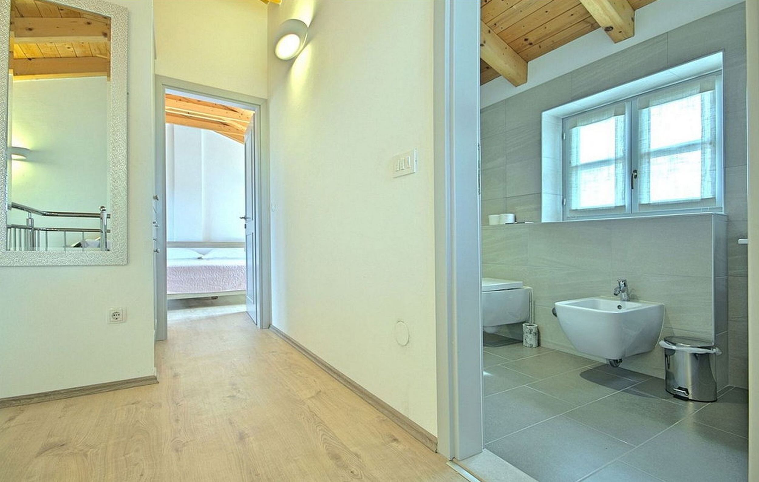 Ein modernes Badezimmer mit Holzboden, einem großen Spiegel, einem Waschbecken und einem Bidet.