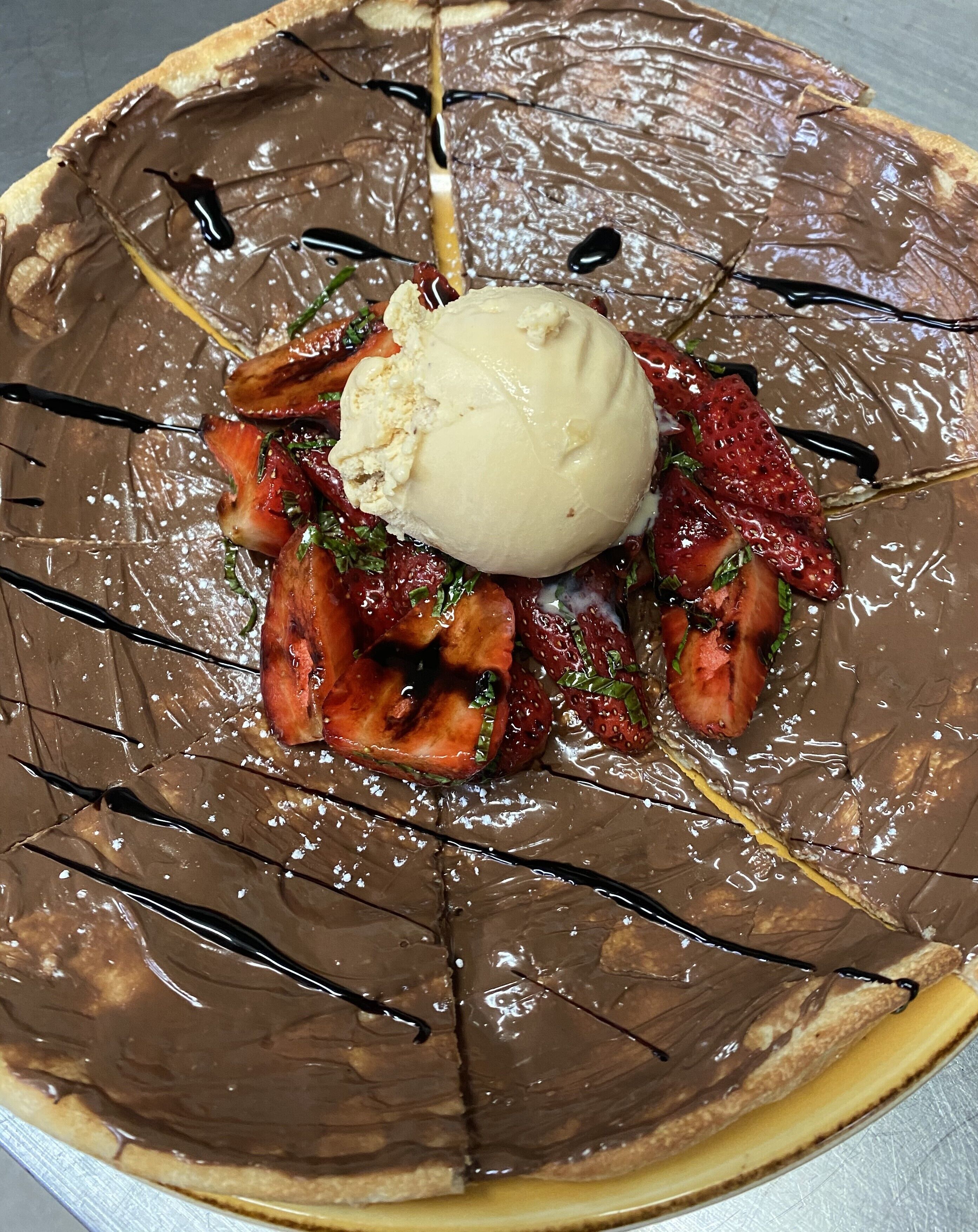 A dessert plate with chocolate sauce, strawberries, and a scoop of ice cream.