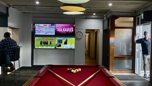 A pool table with a red felt surface, a clock on the wall, and multiple screens displaying sports events. - Tattersall's Hotel Blayney (Blayney)