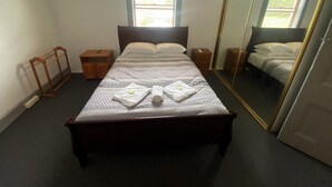 A neatly made bed with a patterned bedspread, a bedside table, a nightstand, a wooden wardrobe, and a large mirror. - Tattersall's Hotel Blayney (Blayney)