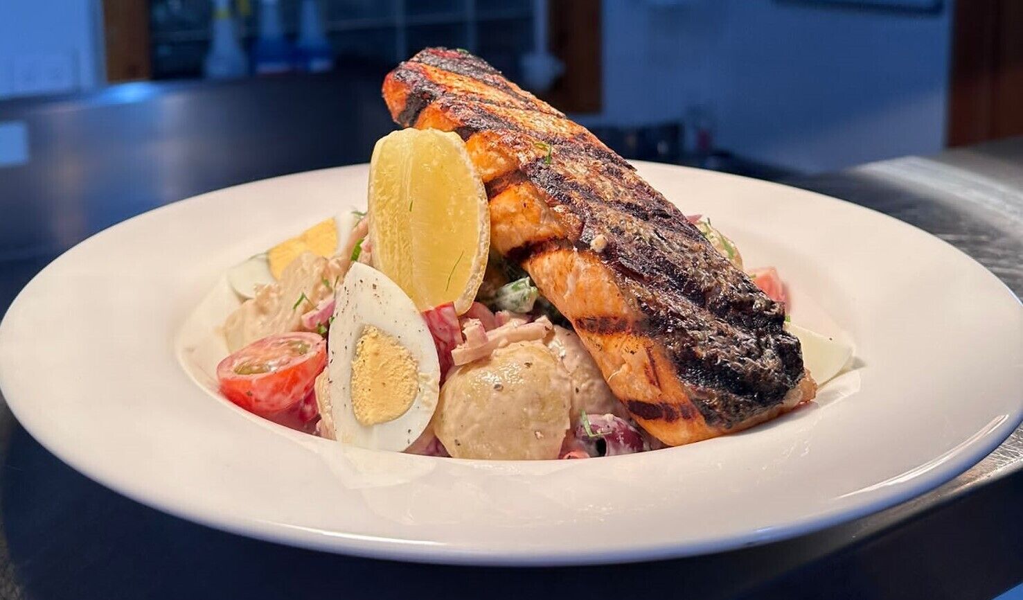A plate with grilled salmon, lemon slices, boiled eggs, and a salad.