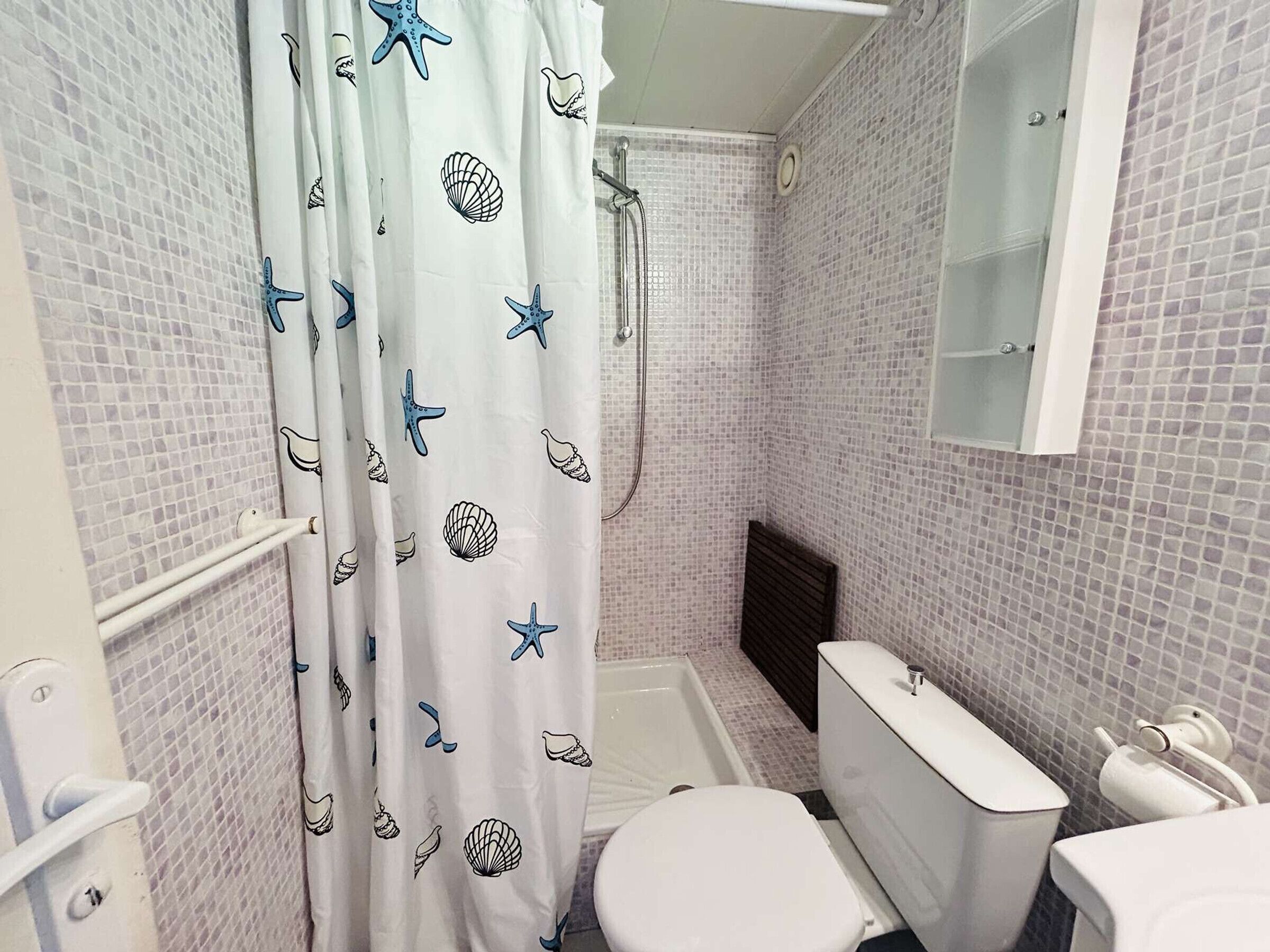 A bathroom with a shower, toilet, and a tiled wall.