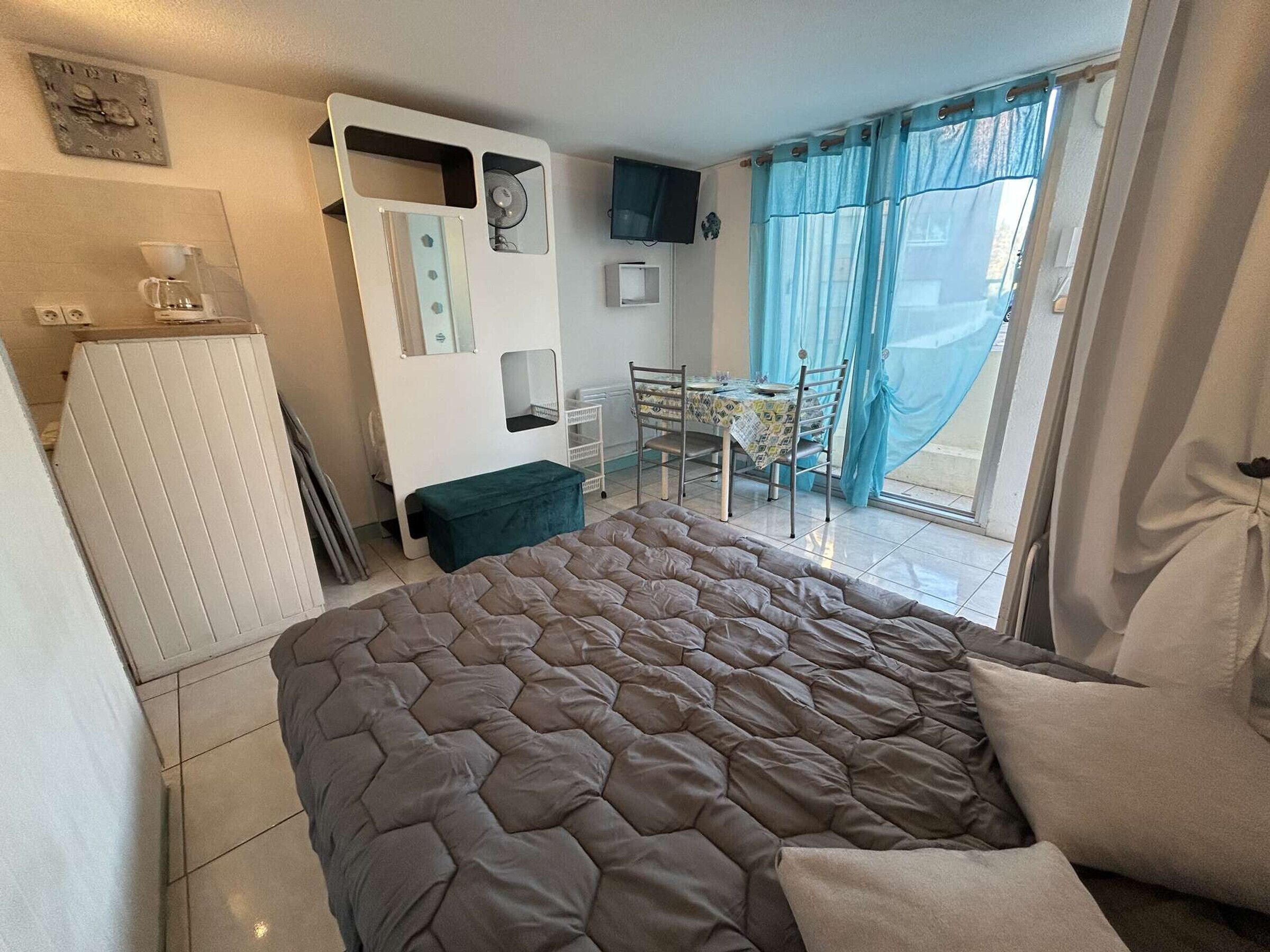 A bedroom with a large bed, a desk with a chair, a small table, and a window with curtains.