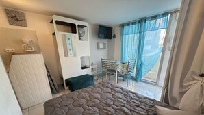A bedroom with a large bed, a desk with a chair, a small table, and a window with curtains. - Renovated Studio in Cap d'Agde by the Beach (Cap d'Agde)