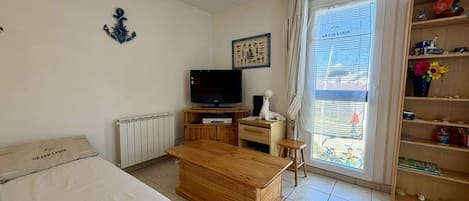 Hotellihuone, jossa on sänky, puinen työpöytä, televisio, patteri, ikkuna verhoilla ja kirjahylly.
