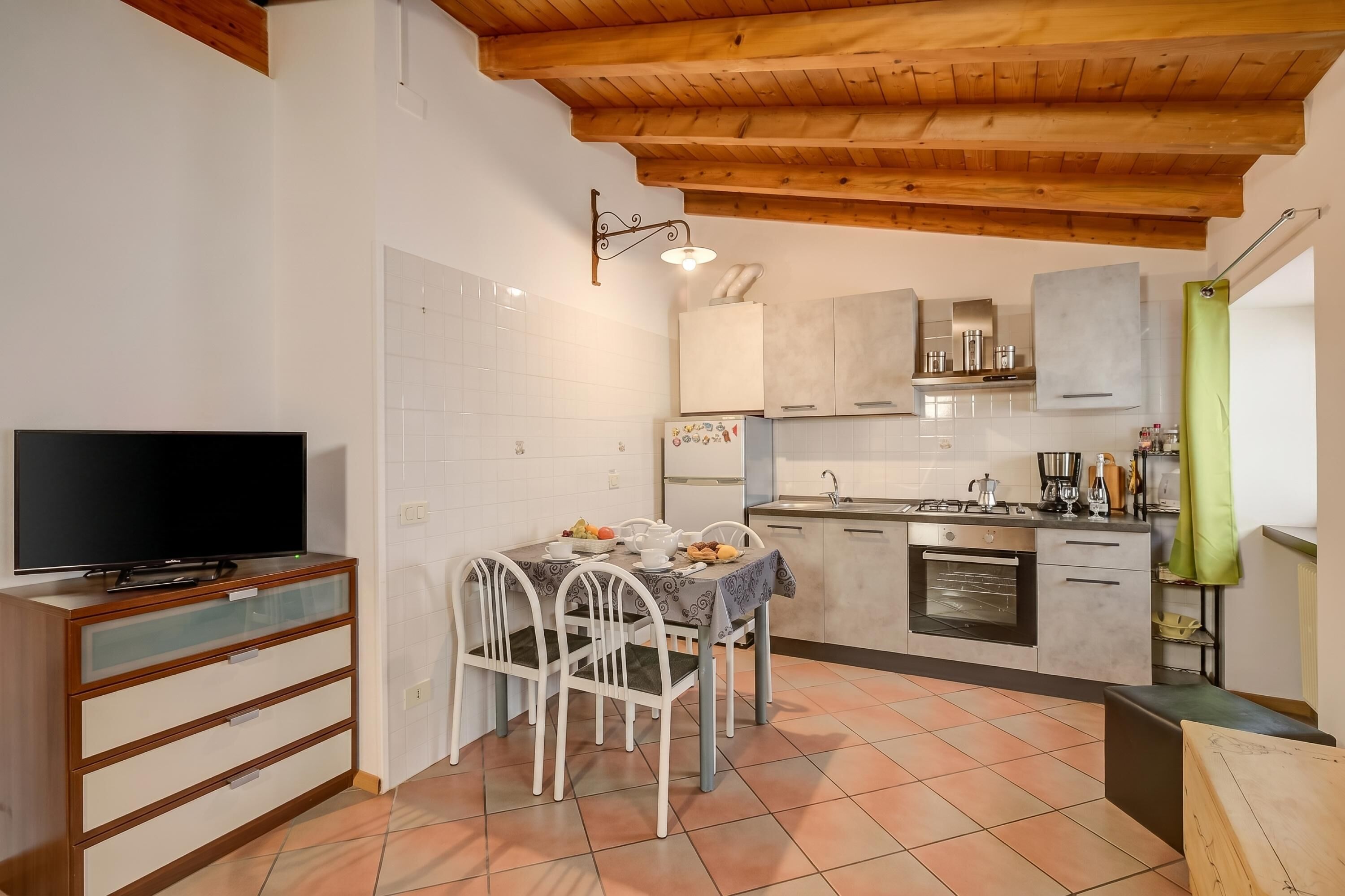 A compact kitchen with a dining table, chairs, a television, and a tiled floor.