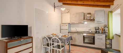 A compact kitchen with a dining table, chairs, a television, and a tiled floor.