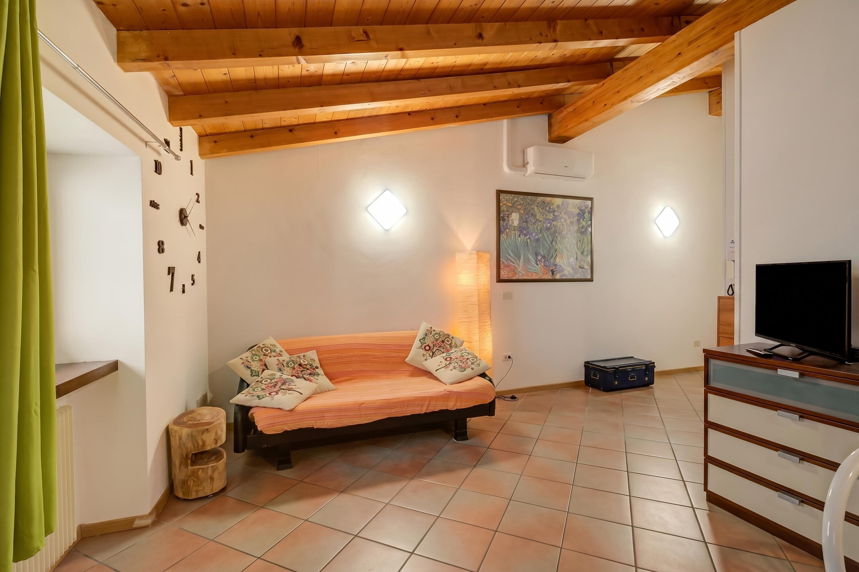 Une pièce avec un plafond en bois, un canapé agrémenté de coussins à motifs, un téléviseur et un tableau accroché au mur.