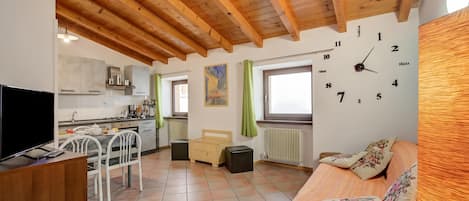 A compact living space with a kitchen, a dining area, a bed, and a wall clock.