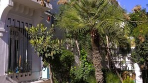 Un edificio blanco con balcones y un jardín bien cuidado con diversas plantas.