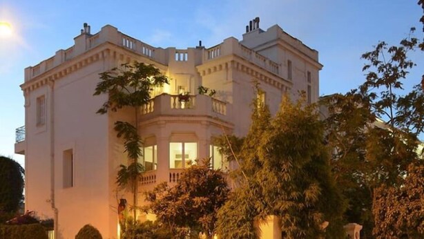 Un edificio grande y blanco de dos pisos con fachada simétrica, varias ventanas y un balcón.