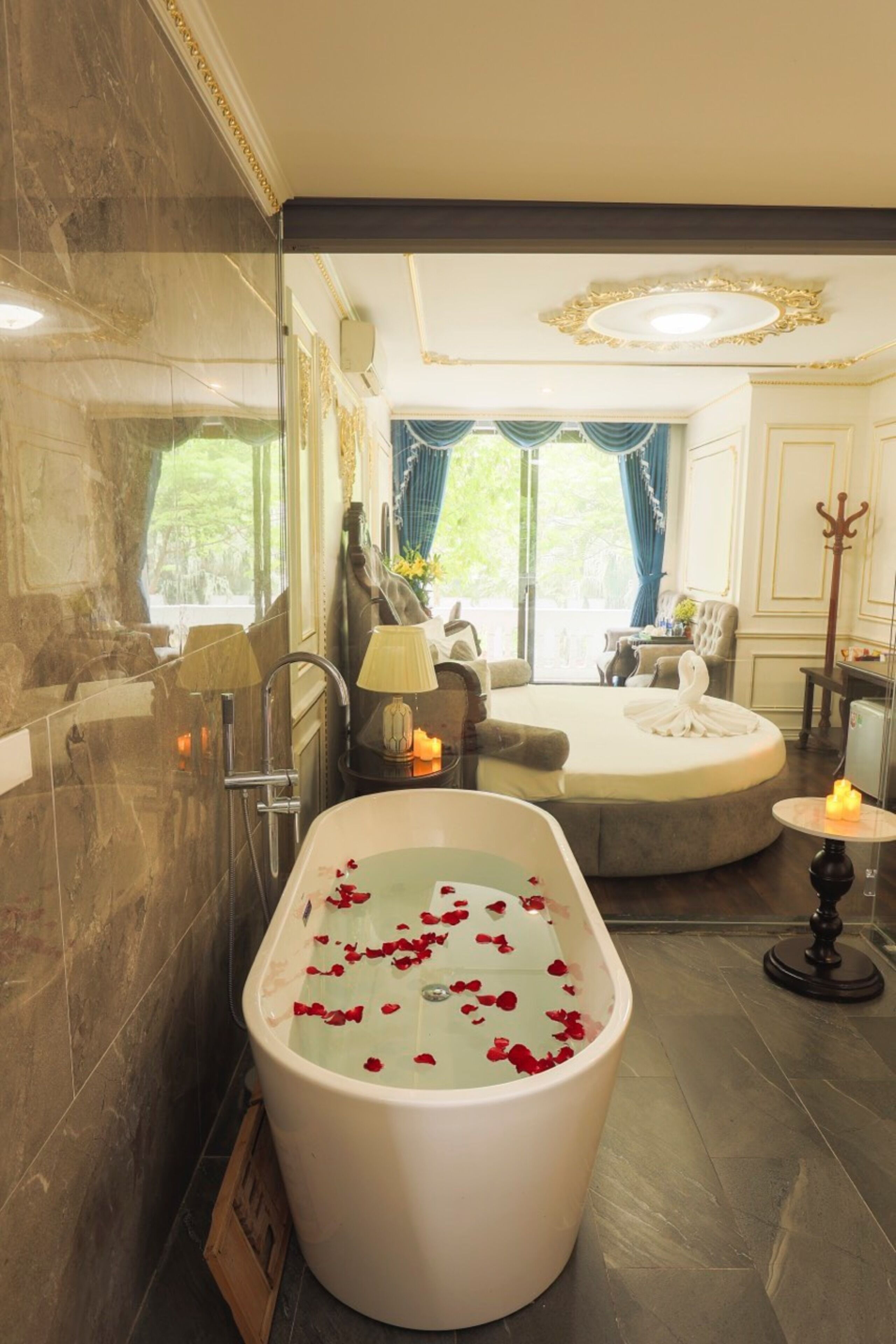 A luxurious bathroom with a freestanding bathtub filled with rose petals, a large mirror, and a view of a garden through the window.