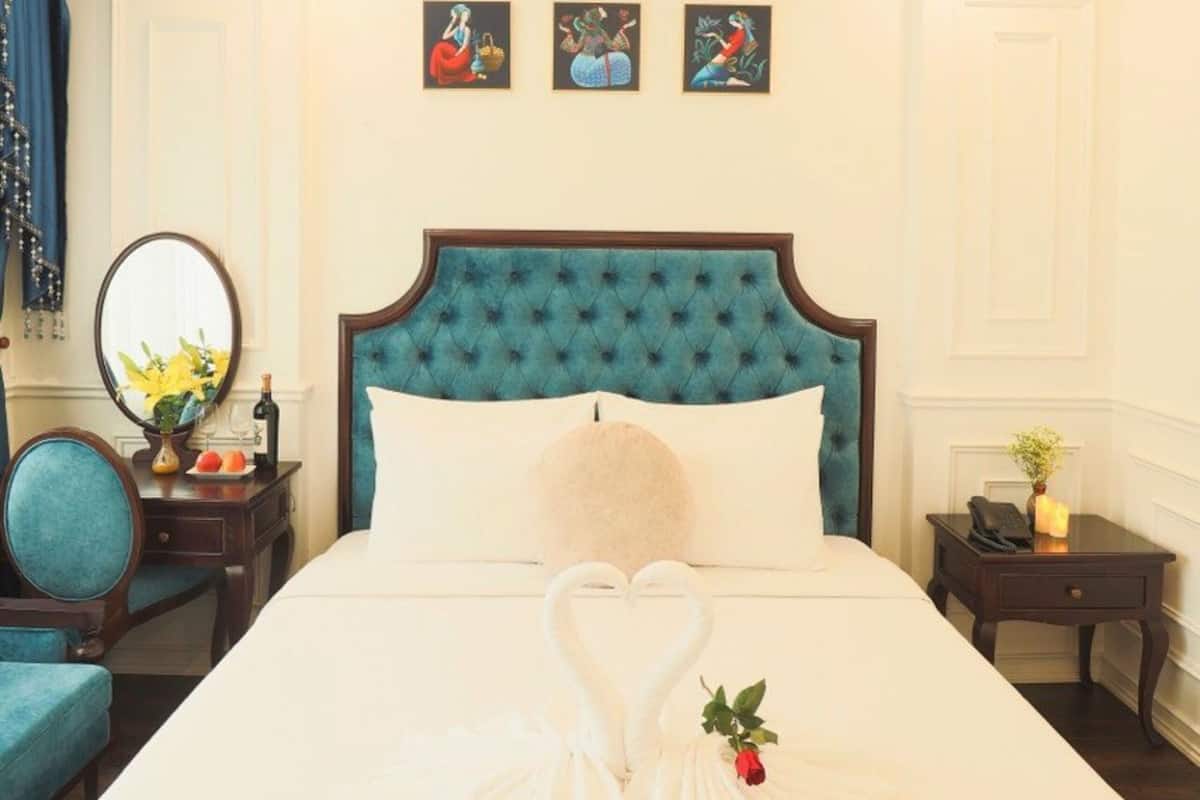 A hotel room with a large bed, a chandelier, a blue upholstered headboard, and artwork on the wall.