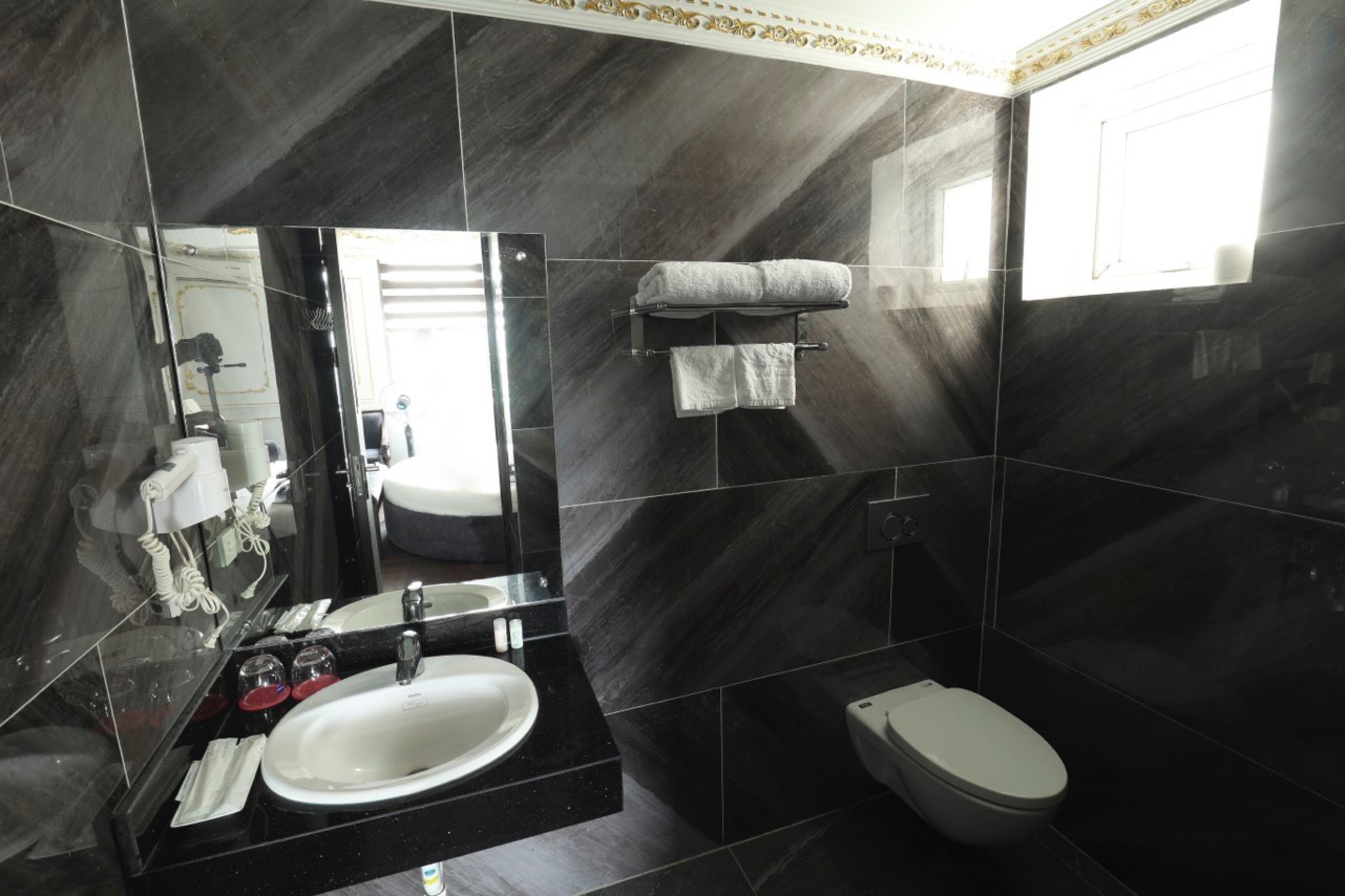 Un baño moderno con un espejo grande, un lavamanos blanco, un inodoro y un perchero para toallas.