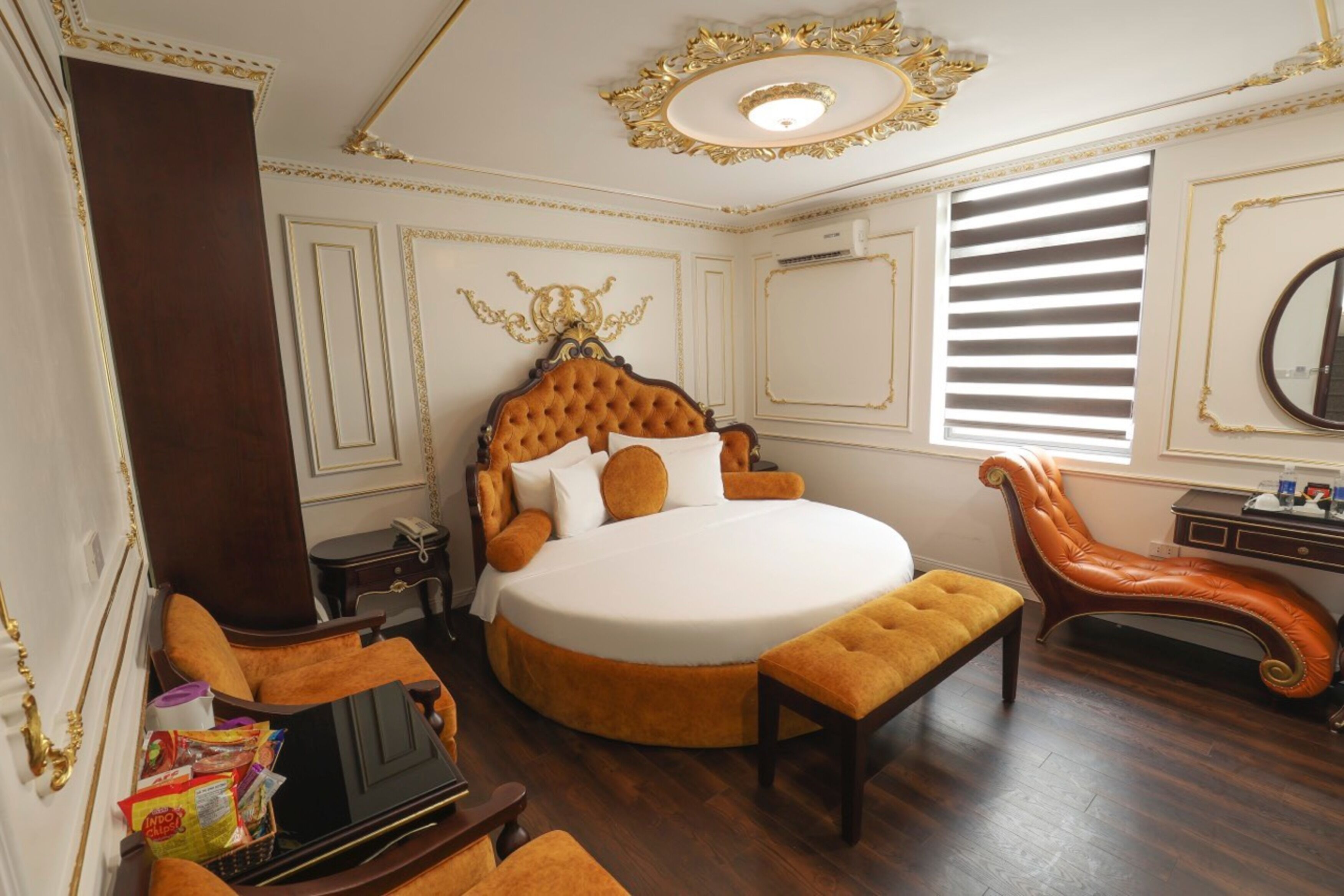 A luxurious bedroom with a large round bed, a chaise lounge, and a wooden nightstand.