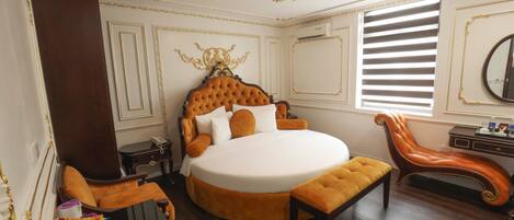 A luxurious bedroom with a large round bed, a chaise lounge, and a wooden nightstand.