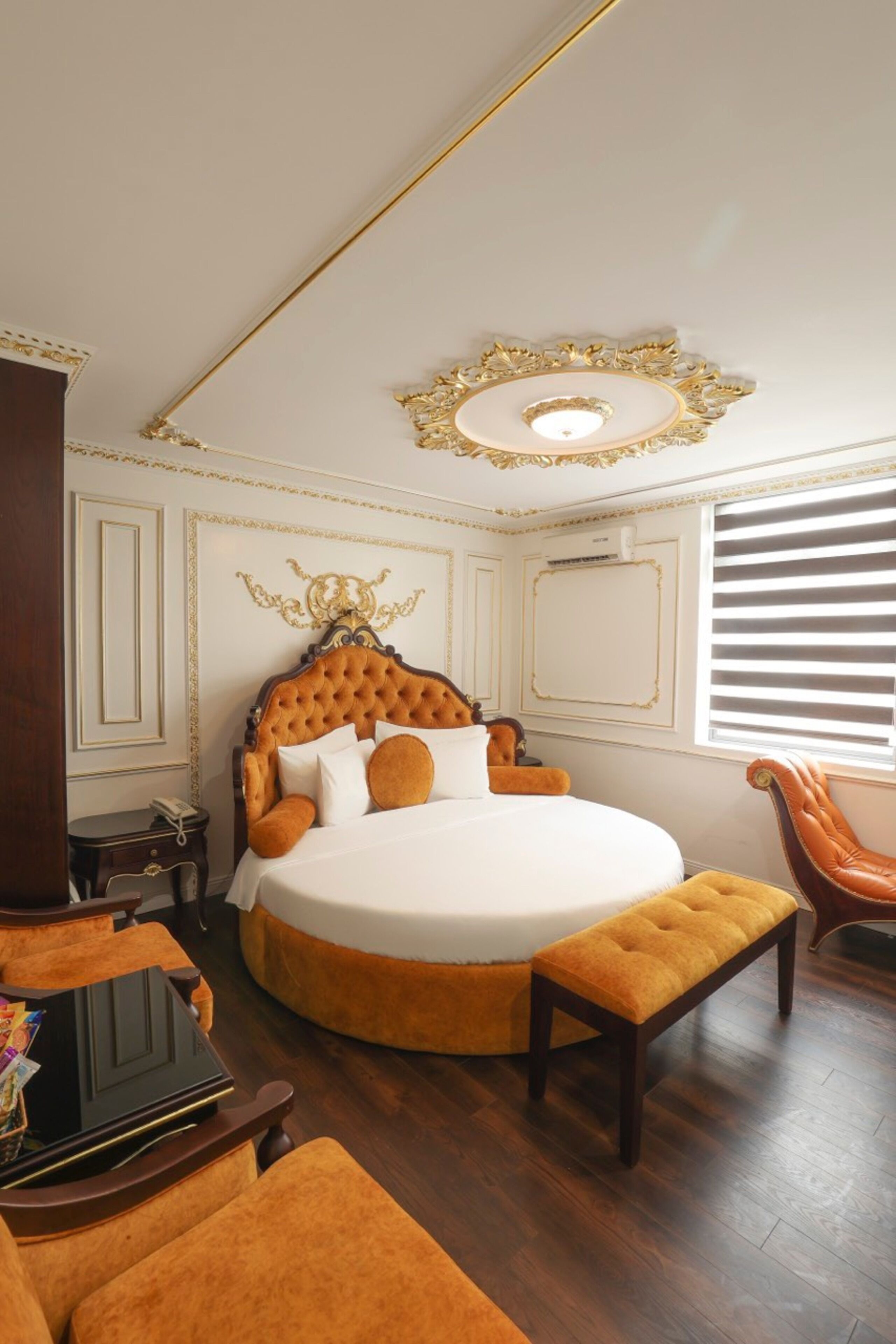 A luxurious bedroom with a tufted headboard, a round bed, a wooden bench, and a chair.
