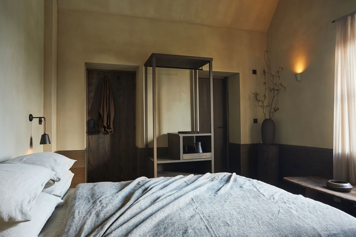Een slaapkamer met een bed, een houten kledingkast, een nachtkastje en een wandlamp.
