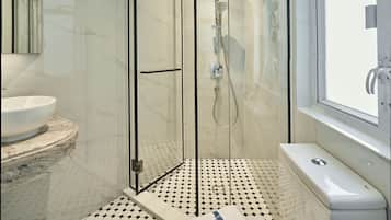 A modern bathroom with a glass-enclosed shower, a white sink, and a toilet with a towel on it.