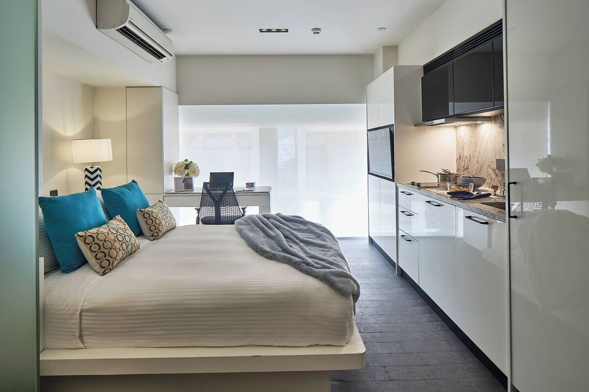 A modern bedroom with a bed, a desk, and a kitchenette.